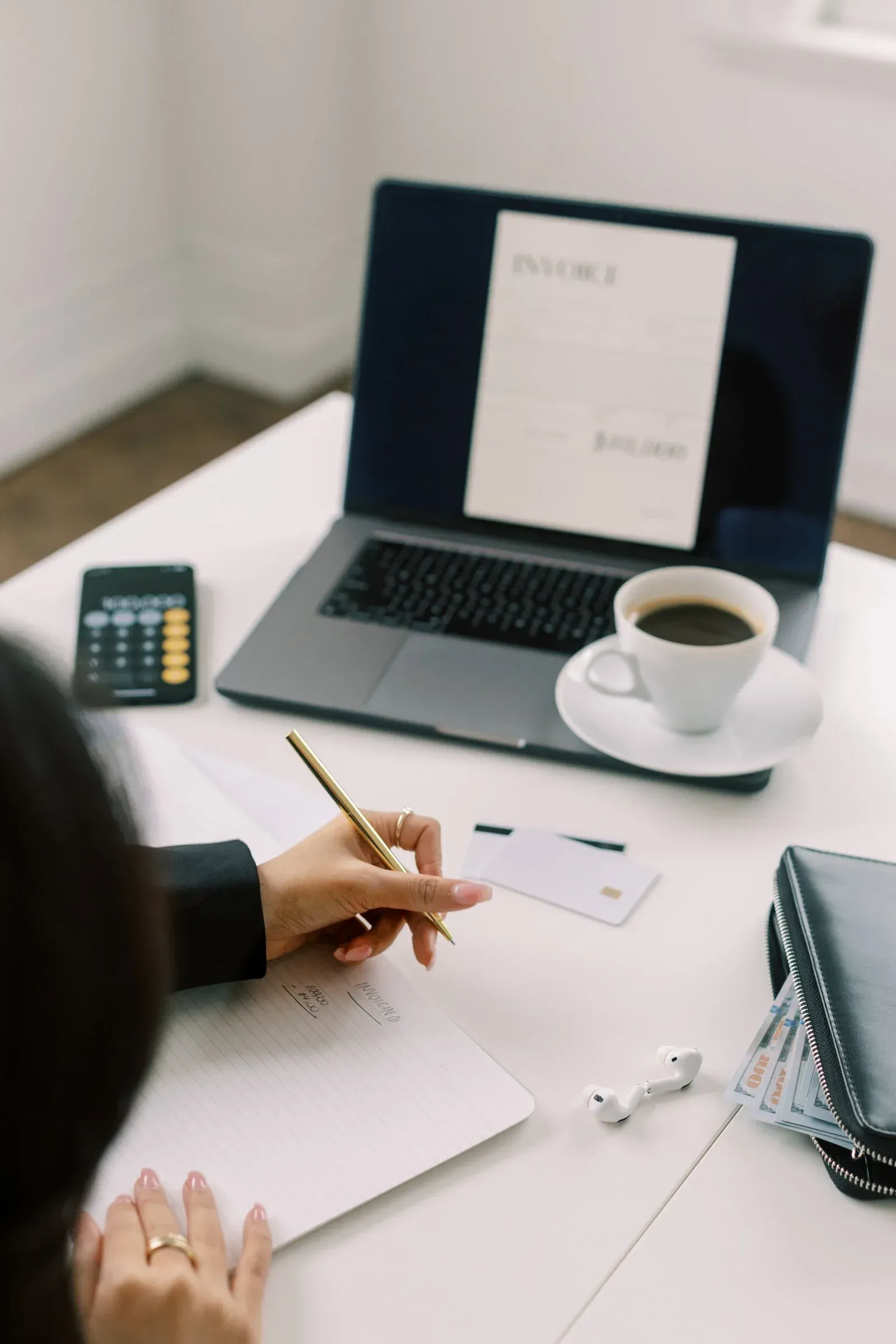 Une indépendante rédige une facture devant son ordinateur, calculatrice et porte-cartes à portée de main